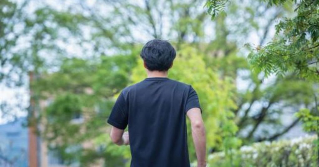 公園の中を一人で歩く男性の後ろ姿。新しい一歩を踏み出すイメージを象徴する写真